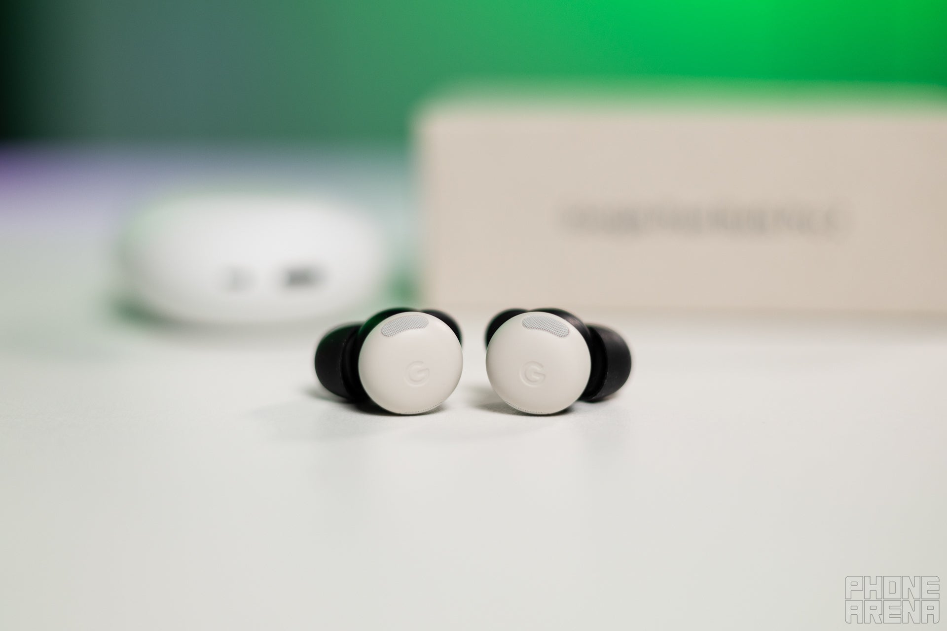 Google Pixel Buds Pro 2 lying on a table, with their charging case and box behind them