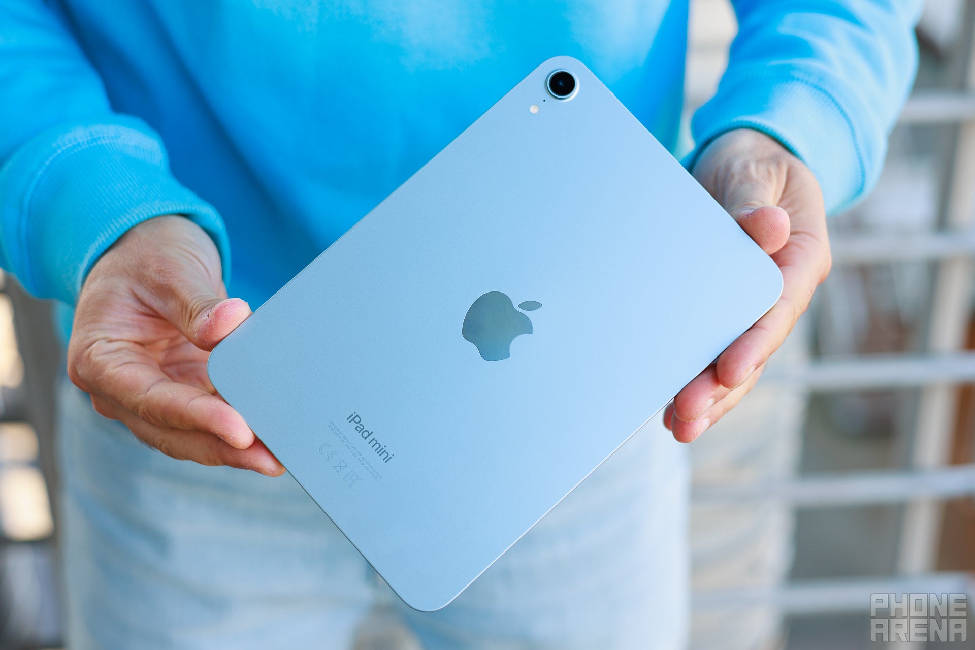 Person holding iPad mini at waist hight, the back of the tablet is towards the camera, showing aluminum build and Apple logo